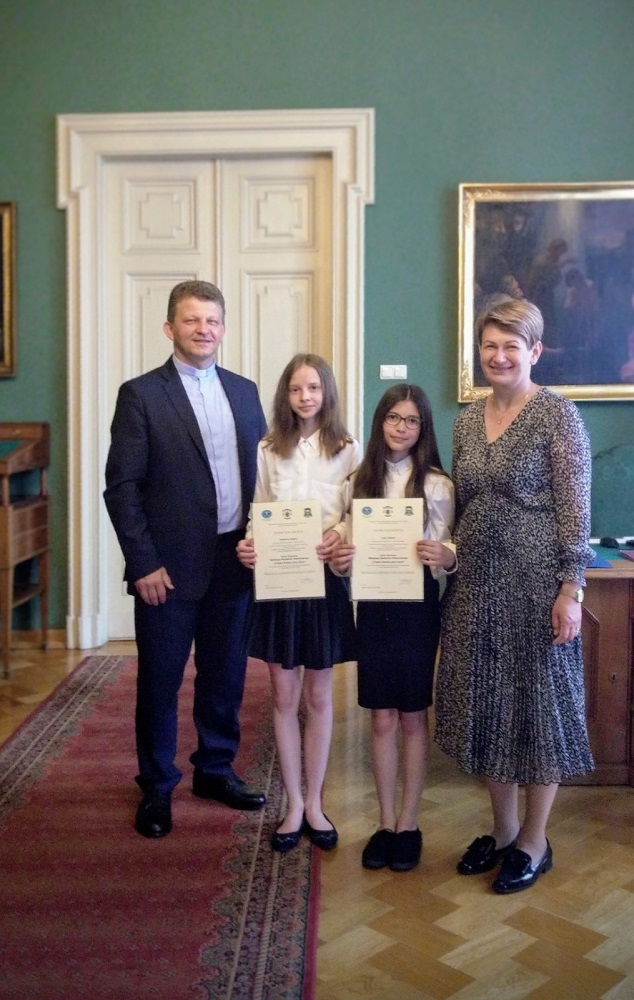 dwie dziewczynki z nauczycielką i księdzem podczas wręczania dyplomów i nagród w Pałacu Biskupim w Krakowie
