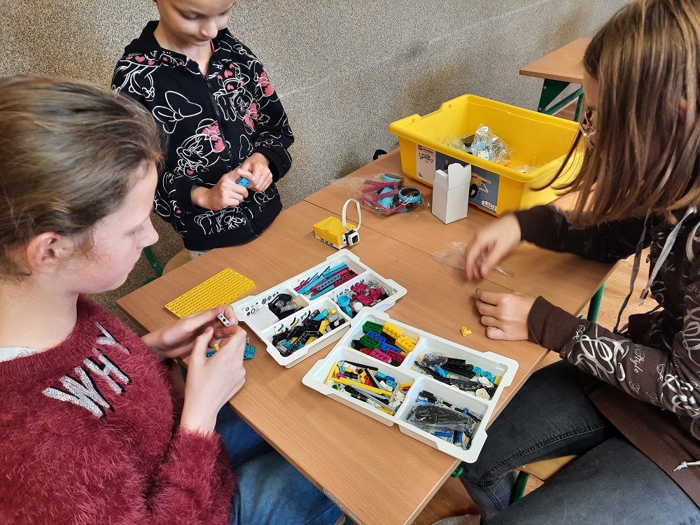 troje uczniów podczas budowania robota z klocków Lego
