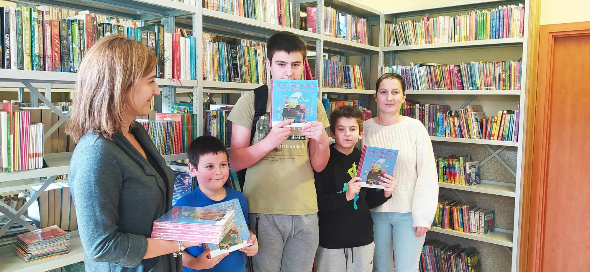 troje uczniów odbierających książki od dyrektora szkoły i pracownika biblioteki